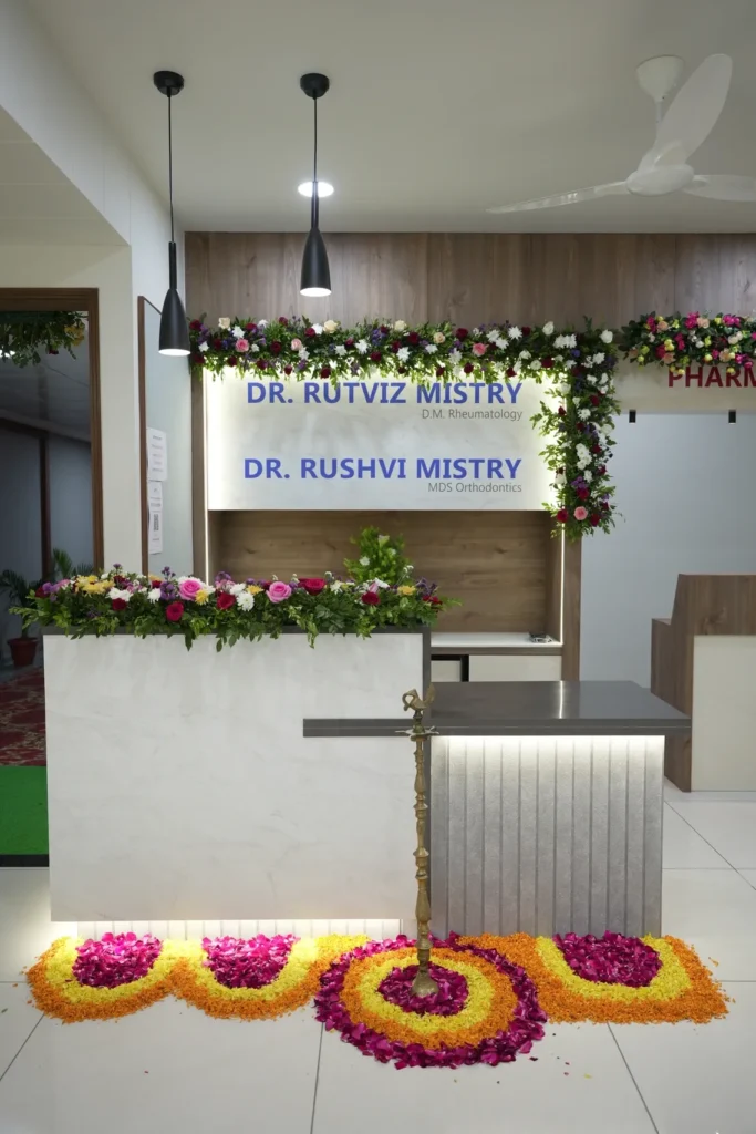 The clinic reception desk decorated with flowers and a floral rangoli, below the Dr. Rutviz Mistry and Dr. Rushvi Mistry name boards