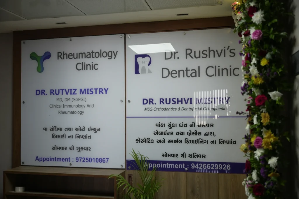 Signboards for Rheumatology Clinic (Dr. Rutviz Mistry) and Dr. Rushvi's Dental Clinic, framed by a floral garland