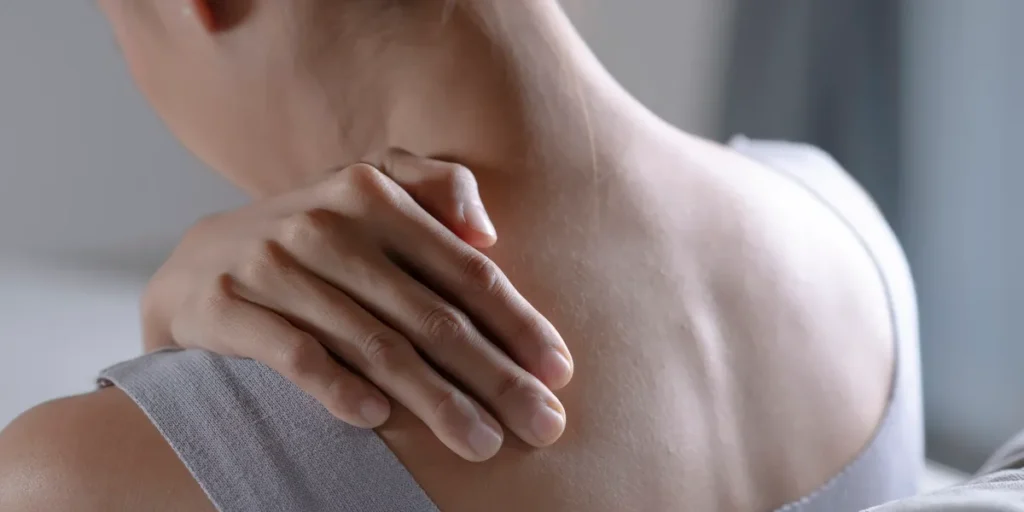 A person resting a hand on their shoulder and neck, suggesting the widespread muscle pain of fibromyalgia