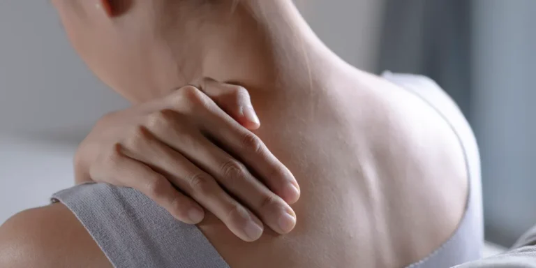 A person resting a hand on their shoulder and neck, suggesting the widespread muscle pain of fibromyalgia