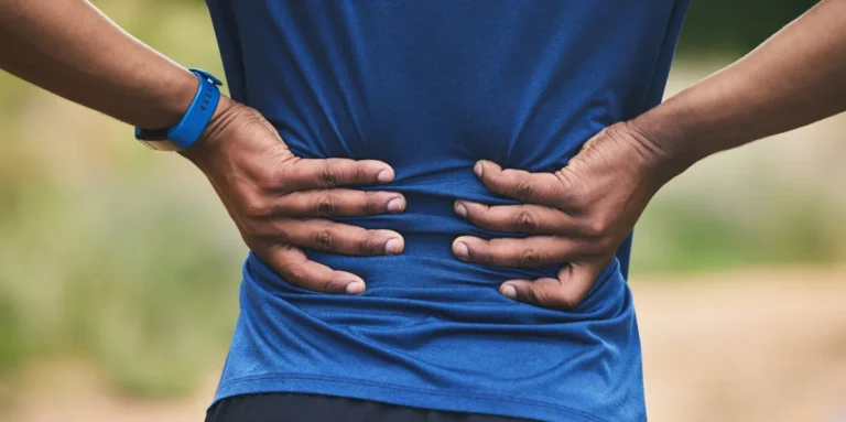 A person seen from behind pressing both hands into their lower back, suggesting inflammatory back pain